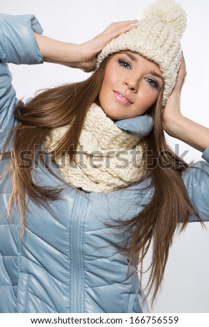 Portrait of a young brunette woman wearing a wool beige cap and scarf and blue jacket