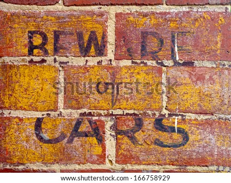 faded yellow and black beware of cars sign on red brick wall