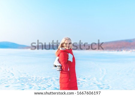 Young beautiful woman in red coat with figure skates stands on the frozen sea early in the morning. Winter outdoor activities concept. Leisure and lifestyle. Background with copy space.    
