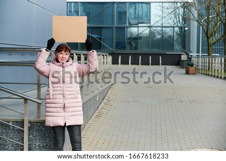 Street photo of a pretty Caucasian woman with a banner in her hands in a pink jacket on a spring day