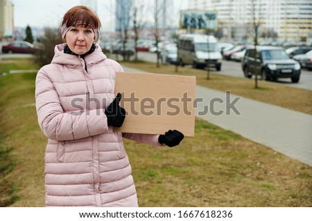 Street photo of a pretty Caucasian woman with a banner in her hands in a pink jacket on a spring day
