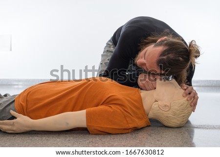 Man teaching cardiopulmonary resuscitation with a dummy on a white background. Checking if the injured person breathes with the maneuver look, listen and feel for signs of breathing(Photo 7 of 18). Royalty-Free Stock Photo #1667630812