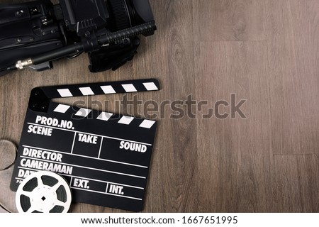 Modern video camera, movie clapper and reel on wooden table, flat lay. Space for text