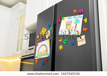 Modern refrigerator with child's drawings, notes and magnets in kitchen