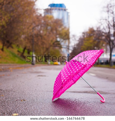 Pink children's umbrella on the wet asphalt outdoors