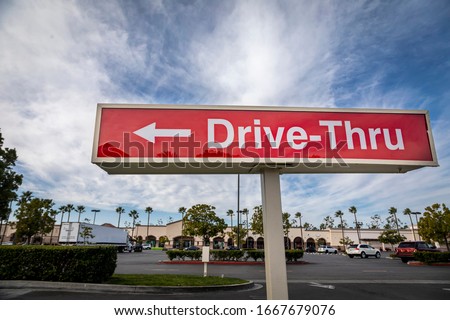 Red rectangular sign reading Drive Thru for fast food retaurant against blue sky and clouds