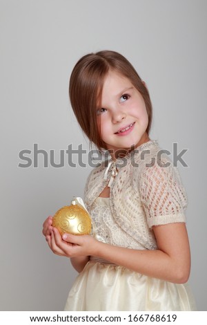 Joyful pretty little girl in a beautiful dress and a cute smile holding a yellow balloon for Christmas tree decorations on a gray background on Holiday