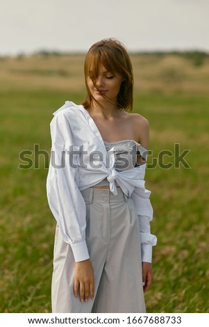 Nice picnic on the grass. Young beautiful woman in the middle of green field chilling and having a good time/ Summer landscape, good weather. Windy day with sun and clouds. Cotton clothes eco style