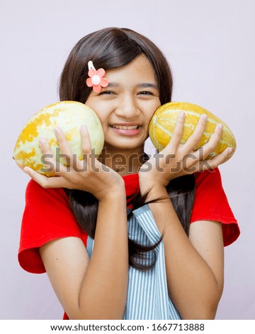 Happy Asian girl hold cantaloupe and wear apron with pink background and copy space.