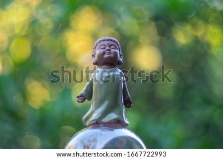 Close up on chinese ceramic young monk doll isolated on blurred bokeh green and yellow background.

