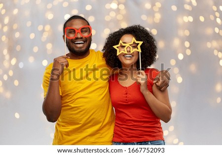 holidays, photo booth and people concept - happy african american couple with party props hugging over festive lights background Royalty-Free Stock Photo #1667752093