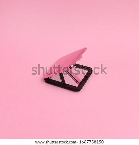 A half open folding hand mirror as a make up accessory on pink background