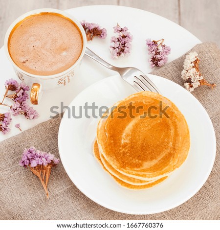 Cup coffee, honey pancakes on plate, flowers and tablecloth on a white coffee table. Gentle good morning. Tasty breakfast