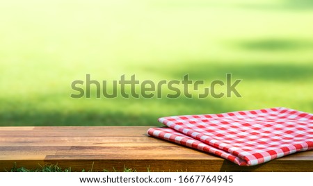 Red checked tablecloth on wood with blur green courtyard background.Summer and picnic concepts.Design for key visual food and drink products.no people Royalty-Free Stock Photo #1667764945