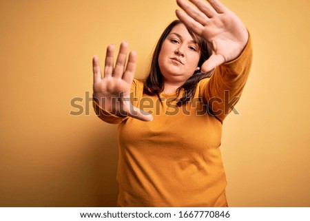 Beautiful brunette plus size woman wearing casual sweater over isolated yellow background doing frame using hands palms and fingers, camera perspective