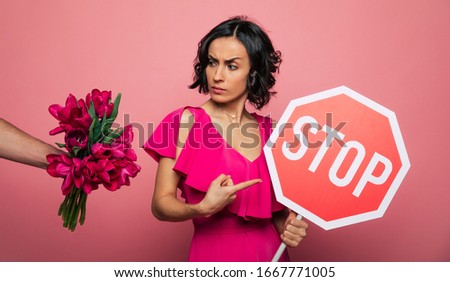 Women rights. Flowers enough. Beautiful stylish serious young woman in a pink dress shows a big red sign of "STOP" in camera.