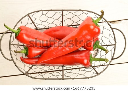 Several ripe organic tasty sweet Kapia peppers, in a metal basket woven from wire, against a background of natural wood painted white.