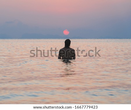 Silhouette of a man standing in the sea and watching the sunset