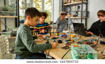 Young technicians building robots and vehicles, using soldering iron to join chips and wires, programming toys at stem robotics class. Inventions and creativity for kids