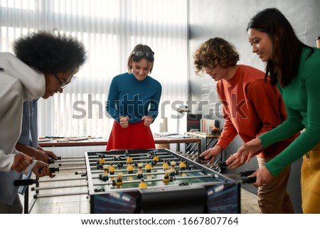 Group of young and happy multicultural people in casual wear playing table soccer in the modern office. Office activities. Having fun together. Happy employees Royalty-Free Stock Photo #1667807764