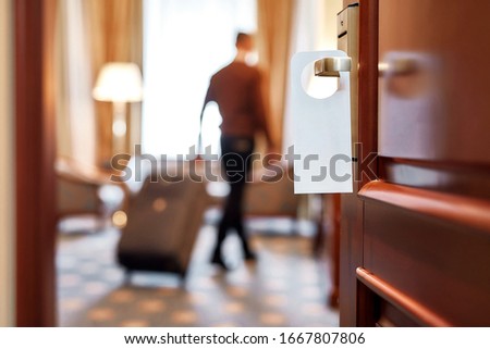 Cropped shot of middle-aged businessman in casual wear with suitcase entering his room in the background. A door with a sign at the front. Horizontal shot. Selective focus Royalty-Free Stock Photo #1667807806