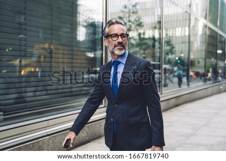 Successful elegant middle aged male executive in expensive suit walking purposefully on New York City street and turning head to side Royalty-Free Stock Photo #1667819740