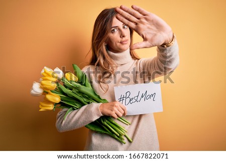 Beautiful brunette woman holding best mom message and tulips celebrating mothers day with open hand doing stop sign with serious and confident expression, defense gesture