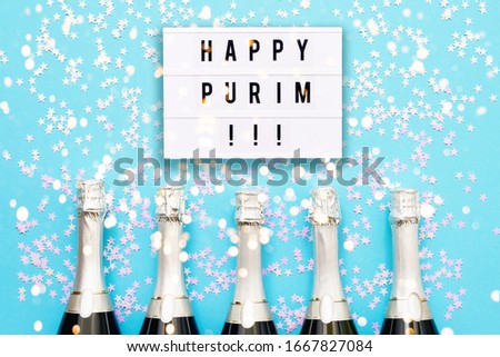 Five Champagne bottles with holographic confetti stars and Happy Purim written in light box on bright blue background. Copy space, top view. Purim celebration concept.