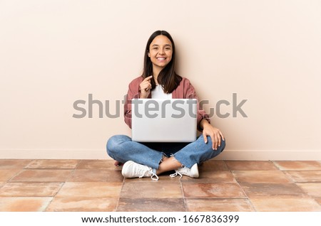 Young mixed race woman with a laptop sitting on the floor showing a sign of silence gesture putting finger in mouth