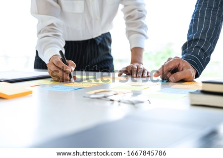 Two creative business people meeting and planning use post it notes sticky note on desk to share idea, Analysis data chart and graph with teamwork strategy brainstorming in office. Royalty-Free Stock Photo #1667845786