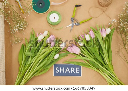 Top view at Spring theme composition with pastel pink tulips on wooden table and SHARE sign in flower shop