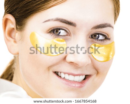 Woman applying golden collagen patches under eyes, on white. Mask removing wrinkles, dark circles. Girl taking care of delicate skin around eye. Beauty treatment.