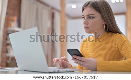 Young Woman using Smartphone and Working on Laptop