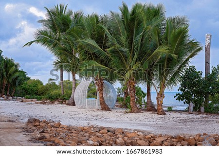 A round cane built white cabana on a tropical sandy beach surrounded by palm trees and with an ocean view