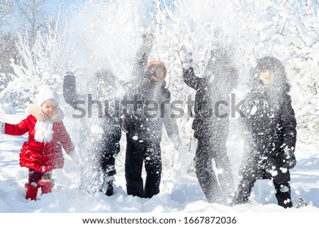 A group of children throw snow and enjoy the winter games in the fresh frosty air. Snow-covered trees behind them. Wonderful winter vacation. Healthy pastime for kids. Four boys and young little girl