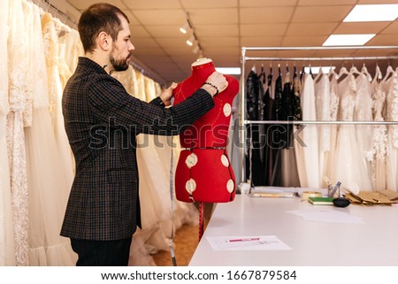 Serious male fashion designer drawing sketch of new clothes collection in ethnic design studio, man tailor creating line, working with brush or pencil on personal desk, developing embroidery pattern