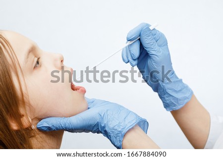 Pediatrician or doctor taking saliva test sample fom elementary age girl's lips performing Saliva testing (Salivaomics)  diagnostic procedure Royalty-Free Stock Photo #1667884090