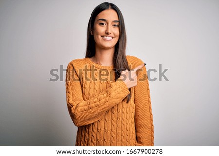 Young beautiful brunette woman wearing casual sweater over isolated white background cheerful with a smile on face pointing with hand and finger up to the side with happy and natural expression