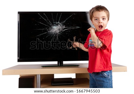 Shocked little boy holding a slingshot standing in front of a TV with broken screen. Home insurance concept. Studio shot isolated on white background.