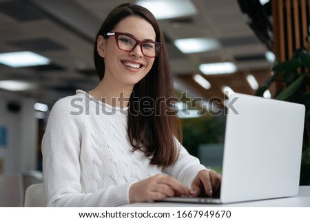 Portrait of happy copywriter working freelance project, typing, looking at camera and smiling. Attractive business woman using laptop computer, sitting in office. Student learning language online