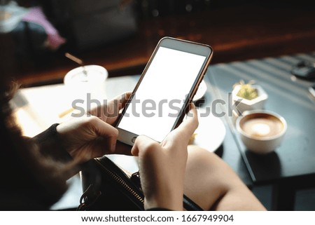 Mockup image of a woman holding and showing black mobile phone with blank screen in cafe