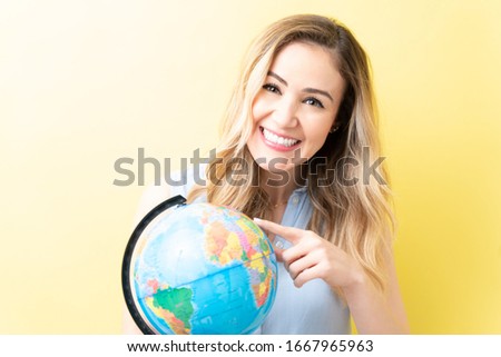 Caucasian woman smiling while pointing at globe against yellow background