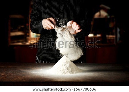 Woman hands in kitchen making food.White flour splash. Dark space and kitchen interior.Copy space for your product. 