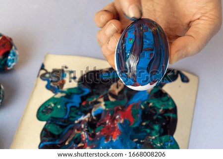 Woman's hands are painting eggs for easter with glowing colours. Decorating eggs with trendy blue colours and abstract paints
