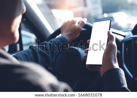 Business man using mobile smart phone, checking address location via navigator application, driving a car. Driver hand holding and looking at cellphone inside a car, white screen mockup