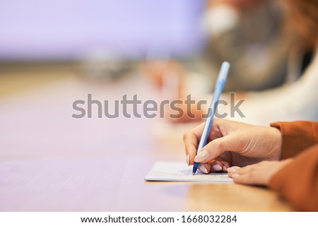 Picture of a human hand writing something on the paper on the foreground