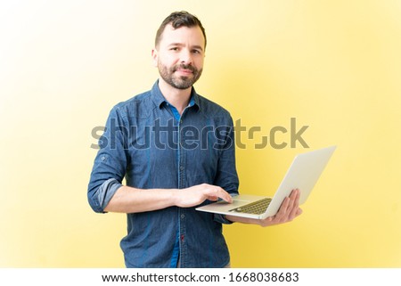 Portrait of confident Hispanic man using laptop against yellow background