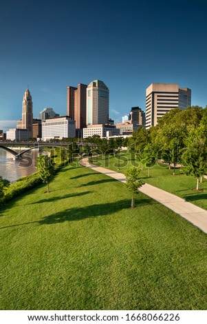 Columbus, Ohio - June 22, 2019:  People walk along the public park path on the Riverfront of the Scioto River by the downtown city skyline and the Discovery Bridge of Columbus Ohio USA
