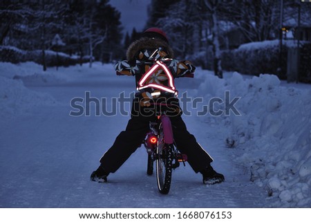 Girl on a bicycle in a winter evening. Light is reflected from clothing reflectors and bicycle wheels. Safe cycling in the dark time. Royalty-Free Stock Photo #1668076153