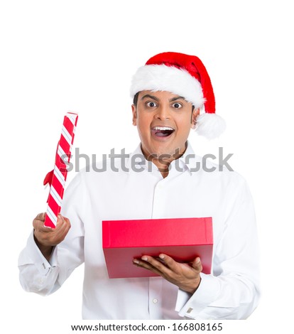 Closeup portrait of handsome young man wearing red santa claus hat, shirt, opening gift and happy at what he gets, isolated on white background, space to left. Positive emotion facial expression